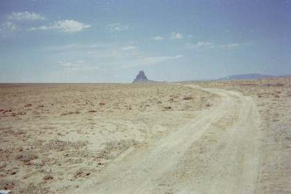 Dirt road across desert with rock formation in the distance