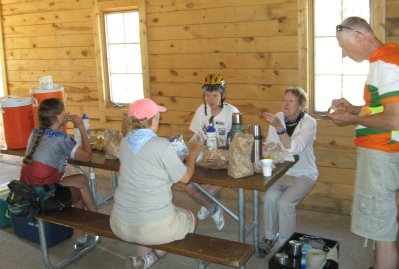 Riders eatingat picnic table inside wood-walled shelter