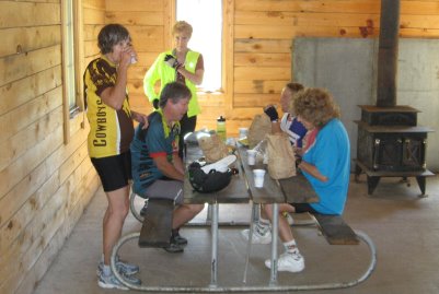 Riders eatingat picnic table inside wood-walled shelter