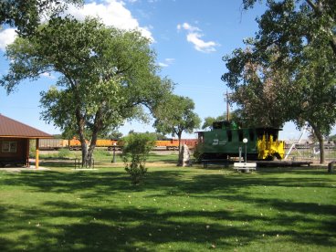 Grassy area with trees, caboose and train on tracks in background