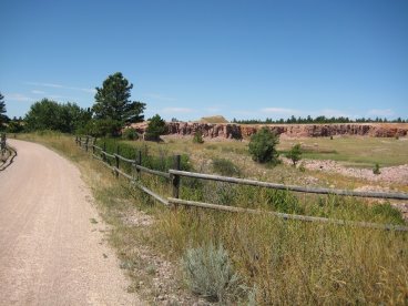 Trail with fence to right and small cliffs in distance