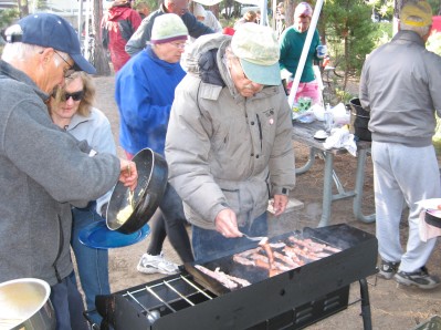 Vin serving eggs from a skillet to Beth while Bob cooks the bacon